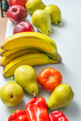 Still life where the curve of the bananas contrasts with the roundness of pears, avocados, potatoes, nectarines, and figs on a light blue background