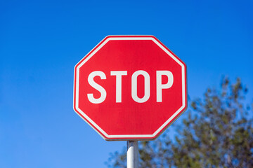 Bright red stop sign against clear blue sky in daylight. Concept of traffic safety and stop...