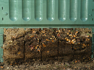 Closeup of green plastic compost bin with lower part removed to show advanced soil decomposition process