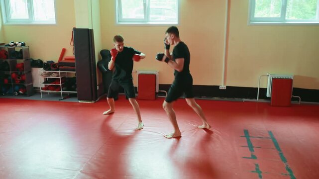 Two wrestlers practicing sparring in gym on red mat, engaged in close combat stance, wearing gloves, barefoot, training martial arts, focusing on power, endurance, agility, discipline, fighting