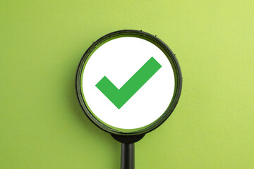 Quality assurance and approval concept. A magnifying glass focuses on a green check mark, symbolizing successful verification, passing a test, and meeting all required standards and compliance.