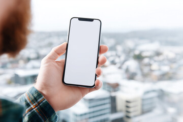 Person holding smartphone mockup with blank screen outdoors in winter city view