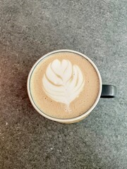 A warm cup of cappuccino with elegant latte art on a gray stone table, captured from above in natural light.