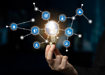 A person holds a glowing light bulb, surrounded by various digital icons symbolizing innovation and...