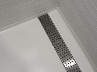 Modern white shower floor with stainless steel linear drain, clean geometric interior design emphasizing minimalism, symmetry, and contemporary bathroom architecture