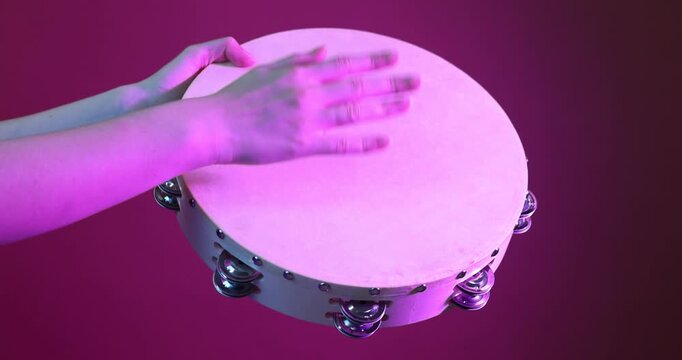 Woman playing tambourine in color light on crimson background, closeup