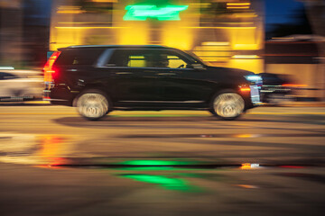 Black executive limo SUV car driving along illuminated wet street at night. Long exposure. Bright colorful neon city lights blurred in background
