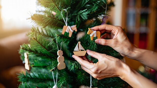 Hands decorating christmas tree with wooden ornaments, adding sailboat and horse shapes, celebrating holiday tradition, sustainable festive decorations, eco friendly christmas spirit