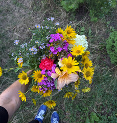 Vibrant bouquet of wildflowers is held by a person in a green field on a sunny day