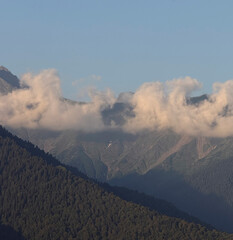 Soft clouds drift over lush green mountains during sunset, creating a peaceful atmosphere