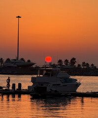 A marina at sunset with boats silhouetted against a bright orange horizon