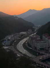 A stunning sunset casts warm colors over a river in a mountain village, illuminating the buildings