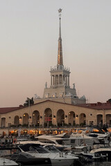 A grand tower stands above a bustling marina filled with yachts near sunset in Sochi