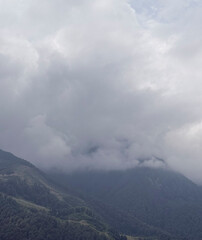 Majestic mountains are shrouded in dense clouds under a gray sky, creating a serene view