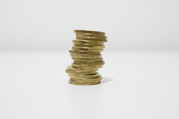 Stack of coins on a white table. Coins stacked in a higgledy piggledy fashion, about to topple over. Investment volatility concept.