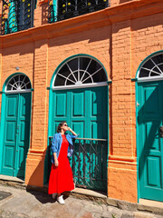 Mature woman in a long red dress leaning against the wall of a brick house