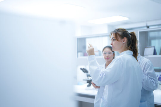 A pathologist presents a challenging case to her colleagues, holding up a histology slide and discussing the cellular morphology to reach a collaborative diagnostic consensus.