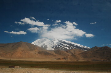 Snow-capped mountain peak under clear blue sky with white clouds