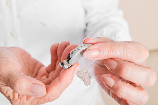 Elderly woman changing hearing aid battery, close-up of hands inserting or removing small power cell from hearing device for senior auditory assistance and maintenance.