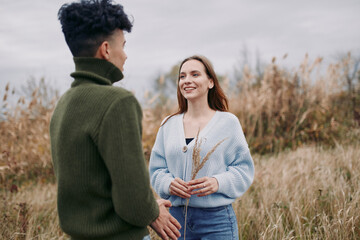 Young couple stands in a windswept meadow sharing a candid moment of genuine connection and honest...