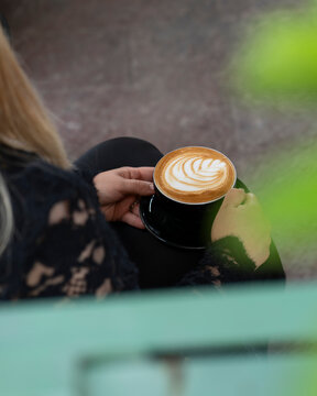 Persona sosteniendo una taza de caf&eacute; latte con arte latte en ambiente acogedor de cafeter&iacute;a