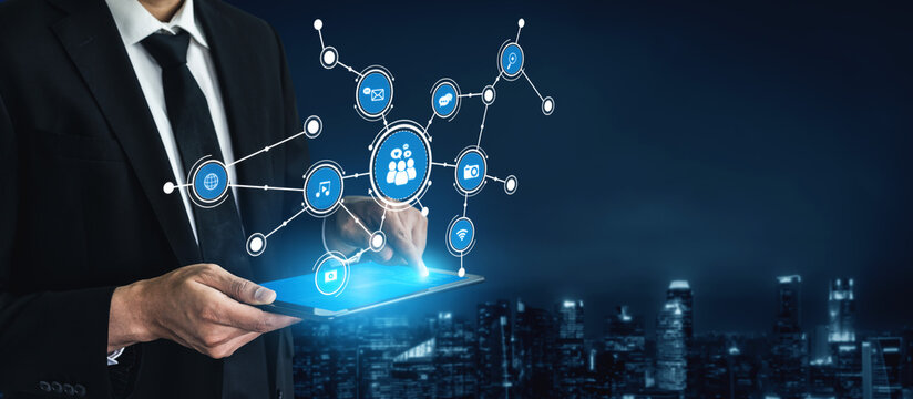 A businessman interacts with digital networks and data visualizations using a tablet, showcasing innovation and connectivity in a vibrant cityscape at night. Tessel - Powered by Adobe