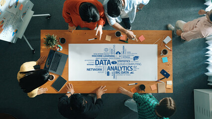 A top-down view of a diverse team engaged in a discussion about data analytics concepts, surrounded by charts and devices in a modern workspace atmosphere. Amity
