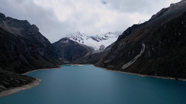 Huaraz, Peru: Tilt down footage of famous laguna paron in Caraz, Huaraz region, Peru. Surrounded by mountain range and with cloudy dramatic sky, showing cordillera blanca in the background