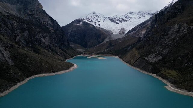 Huaraz, Peru: Tilt down footage of famous laguna paron in Caraz, Huaraz region, Peru. Surrounded by mountain range and with cloudy dramatic sky, showing cordillera blanca in the background