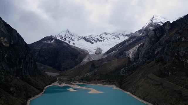 Huaraz, Peru: Aerial drone footage of the famous Lake paron in the Cordillera blanca in the Peruvian Andes mountain. With forward and tilt down motion from drone, showing the lagoon under dramatic sky