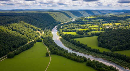 Aerial view of a lush green valley with a winding river flowing through it on a sunny day, creating a picturesque and tranquil landscape