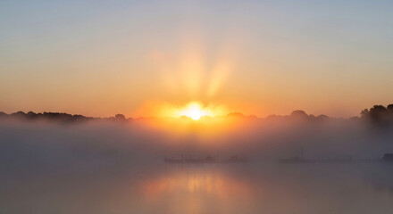 Fototapeta premium A breathtaking sunrise over a tranquil lake, with the suns golden rays piercing through the morning mist and creating a serene and ethereal atmosphere