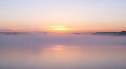 Obraz premium The tranquil lake is shrouded in a mystical fog, with the soft pastel colors of the sunrise creating a serene and ethereal atmosphere