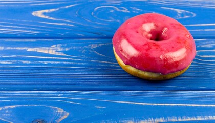 A glazed doughnut sits atop a vibrant, textured blue wooden surface, bathed in natural light. The pastry is close-up and center