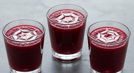 Three Glasses of Red Juice with White Decorative Star Pattern Served in Clear Glass Cups on Gray Surface