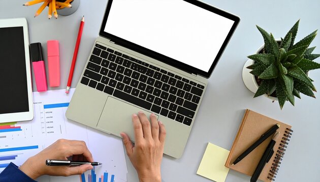 Overhead view of a person working on a laptop and analyzing documents with charts at a modern office desk.