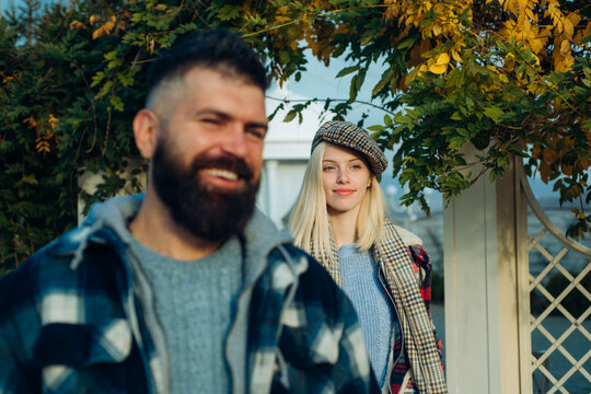 Disfocused bearded smiling man and beautiful blonde woman standing under colorful autumnal leaves. Romantic hipster stylish couple walk at autumnal garden and have fun.