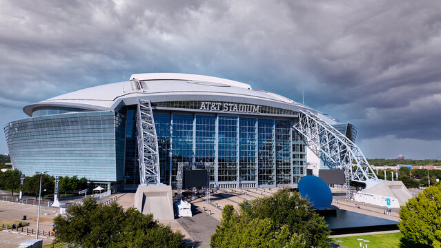 Aerial drone photo of AT&T Stadium in Arlington, Texas, with dramatic sky. The image captures the stadium&rsquo;s modern architectural design with its iconic retractable roof, massive glass fa&ccedil;ade. 