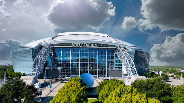 Aerial drone photo of AT&T Stadium in Arlington, Texas, with dramatic sky. The image captures the stadium&rsquo;s modern architectural design with its iconic retractable roof, massive glass fa&ccedil;ade. 
