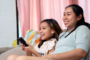 Asian Mother and Daughter Smiling and Watching TV Together at Home
