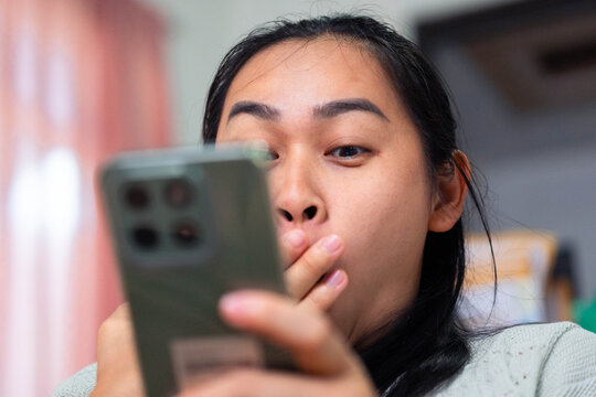 Asian Woman Shocked and Covering Mouth While Looking at Smartphone - Powered by Adobe