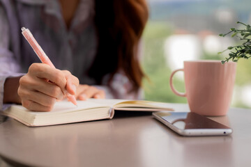 Adult Asian woman hands write personal journal notebook goal planning serene home office balcony morning routine productive day remote worker new ideas