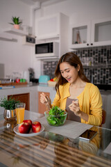 Asian woman adult eats fresh green salad healthy meal kitchen dining table home modern lifestyle well-being nutrition conscious eating