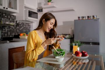 Asian woman capturing fresh vegetable salad meal for healthy lifestyle content at home kitchen dining table