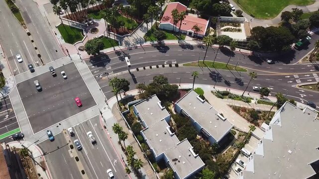 Above a coastal boulevard intersection in Redondo Beach while panning to palm lined streets apartments and park space on a bright late August day. Clean traffic patterns and urban infrastructure