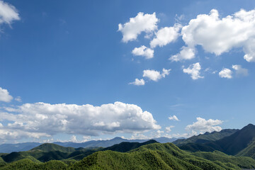 Fototapeta premium Blue Sky with White Clouds Over Green Mountain Ranges