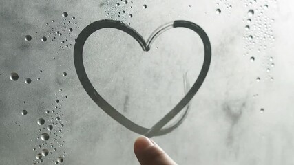 Finger drawing on a steamy glass surface creating a sense of mystery and anticipation with blurred motion and water droplets