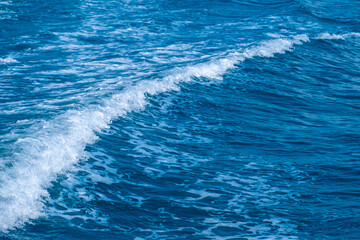 Dark blue and white ocean waves form diagonal lines on the sea surface, with fine white foam contrasting against the rippling water, demonstrating the power and movement of the ocean.