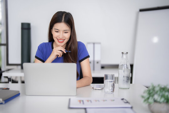 Asian businesswoman casual remote work on laptop in bright modern office setting professional productivity and cheerful focused happy work