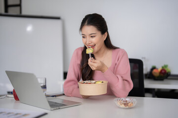 Asian adult businesswoman enjoys healthy lunch break remote working on laptop computer at home office for productivity